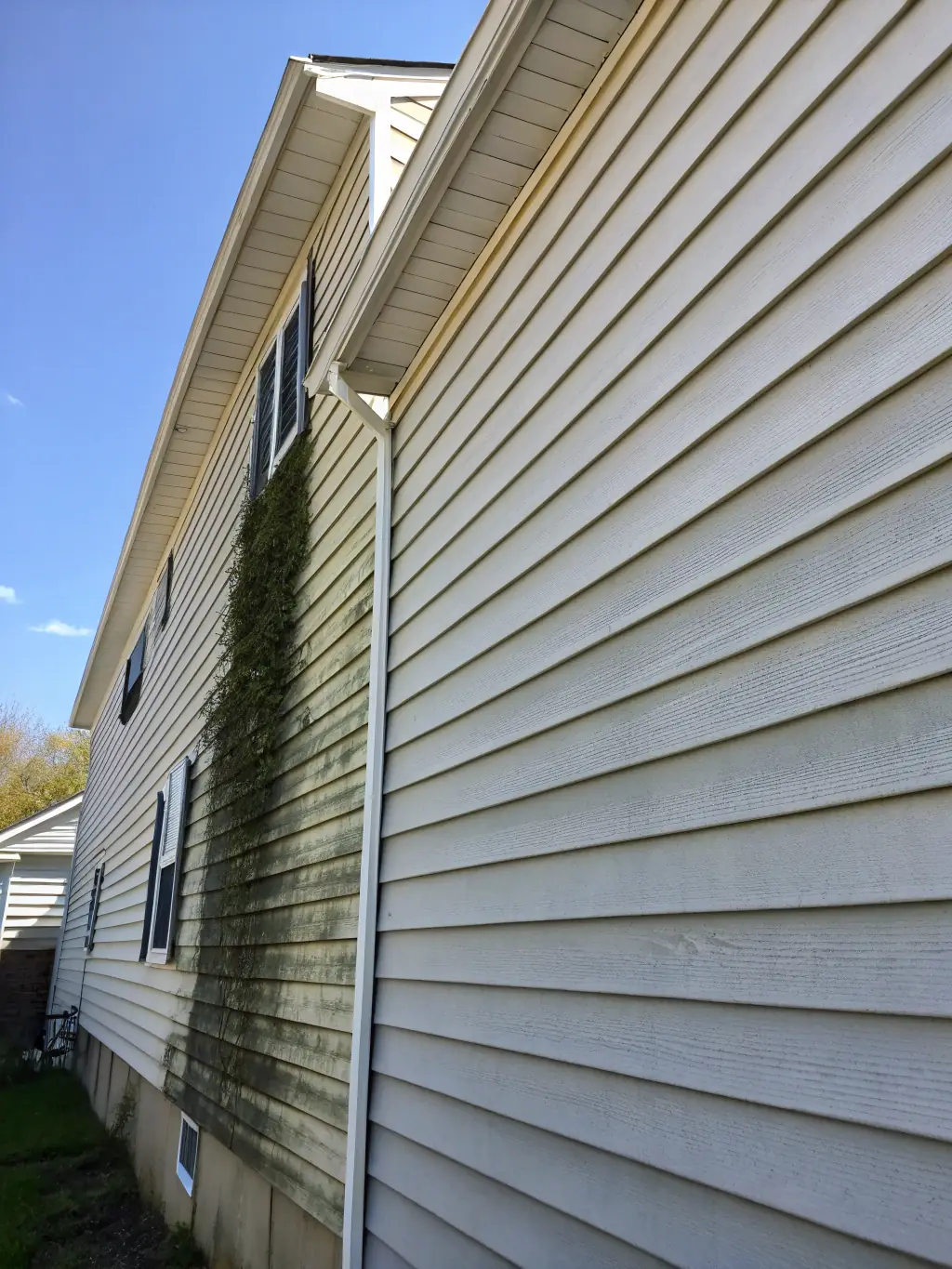A photo of a house with a clearly dirty exterior, half of which has been pressure washed to look clean and new, demonstrating the dramatic before-and-after effect of Outdoor Pros' services.